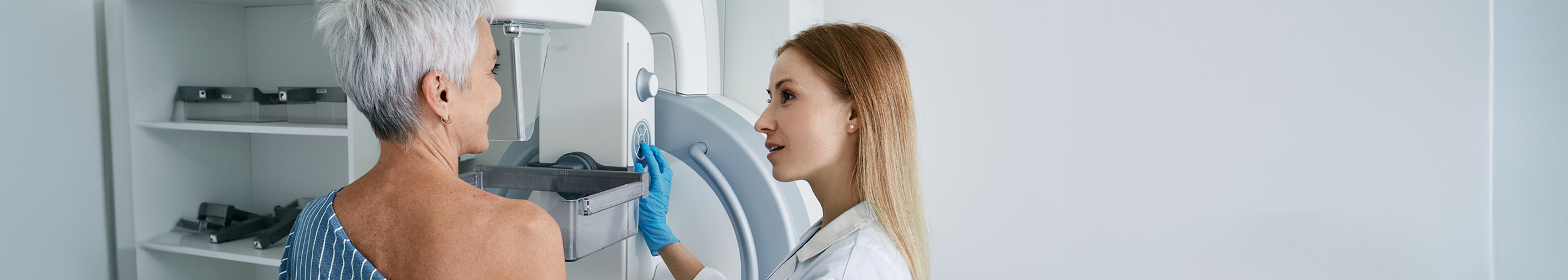 A female radiographer supporting a woman in her 50s while she has a mammogram.