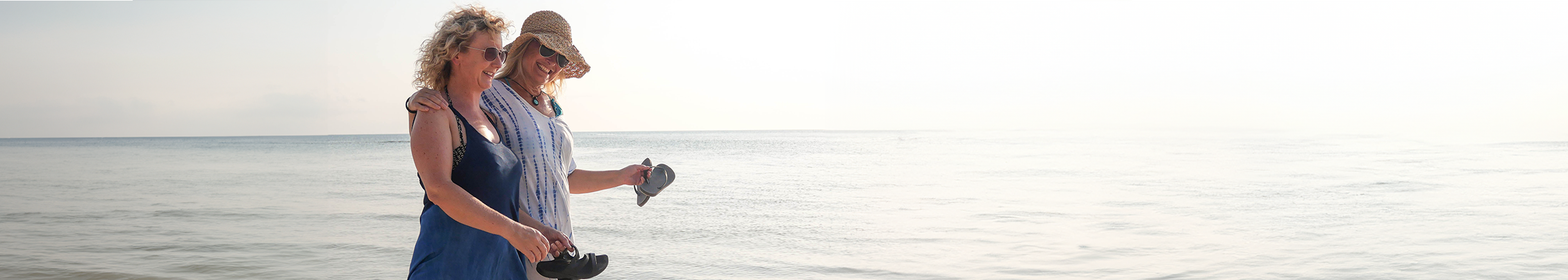 Two happy, empowered women in their 50s walking on the beach, possibly discussing a BreastScreen appointment.