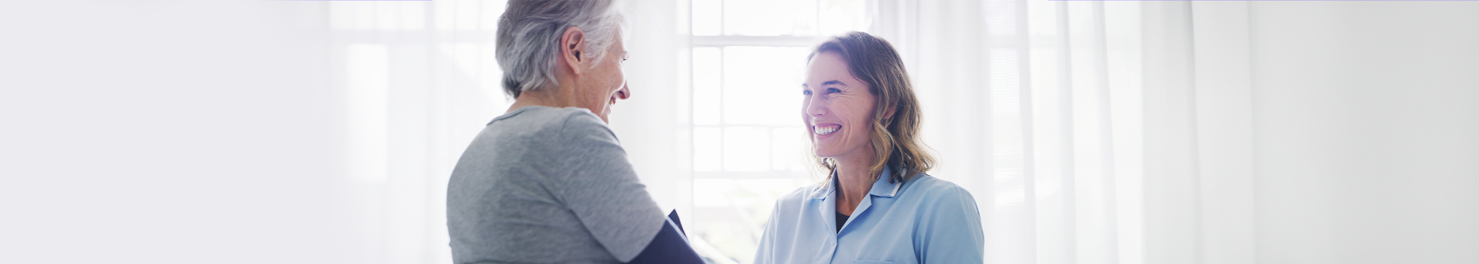 Two women smiling as they greet each other, possibly at a breast screen appointment.